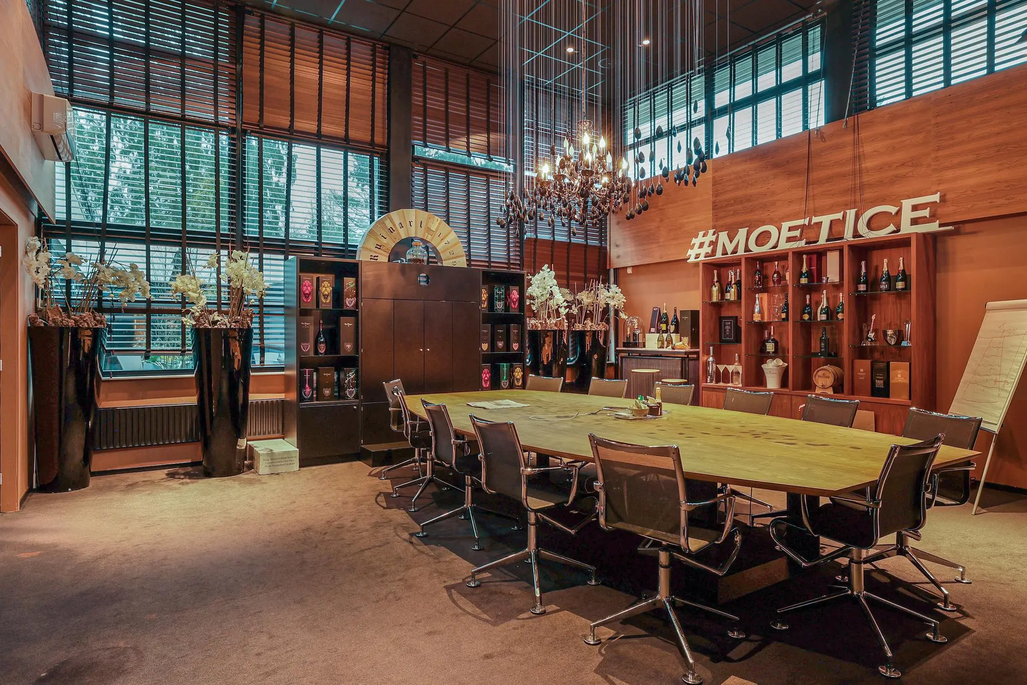 Vergaderruimte aan de Oude Utrechtseweg met een lange tafel, moderne stoelen, luxe decoratie en een wand vol champagneflessen onder de hashtag #MOETICE.